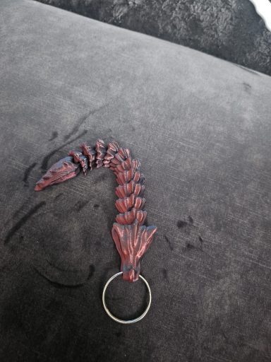 Rode sleutelhanger in de vorm van een slang of draak op een zwarte ondergrond.